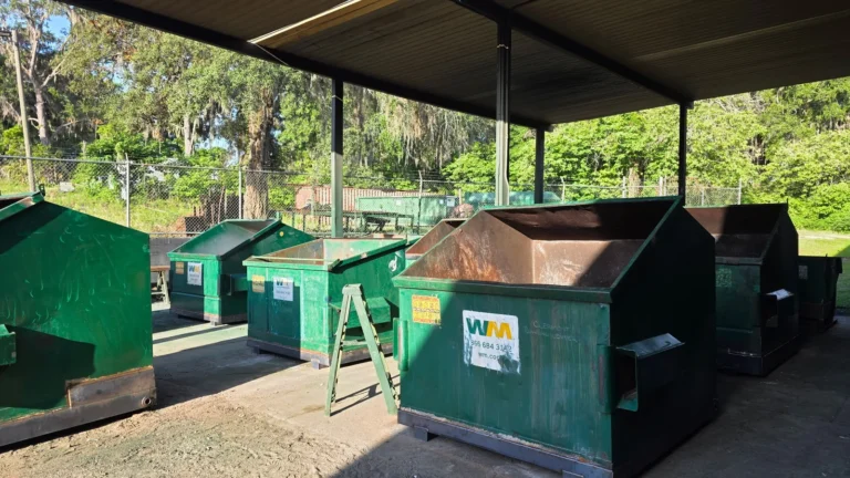 Green front-load dumpsters at North Florida Container shop awaiting repair