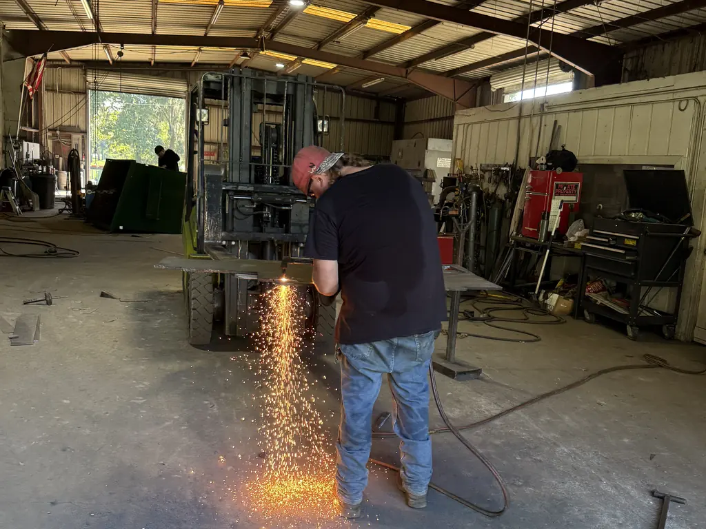 Technician plasma-cutting new steel plate for a dumpster repair inside the NFC shop in Ocala, sparks flying