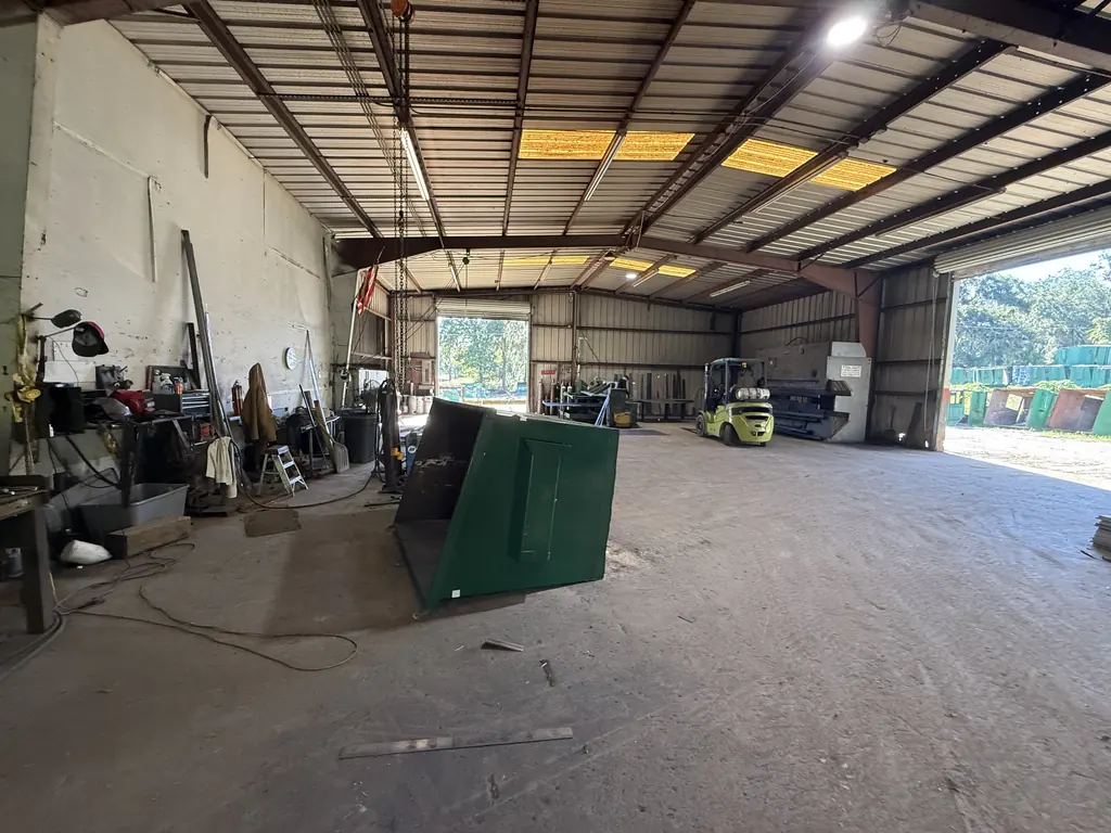 Inside the North Florida Container repair shop in Ocala with a front-load dumpster tipped for floor work and a forklift in the bay