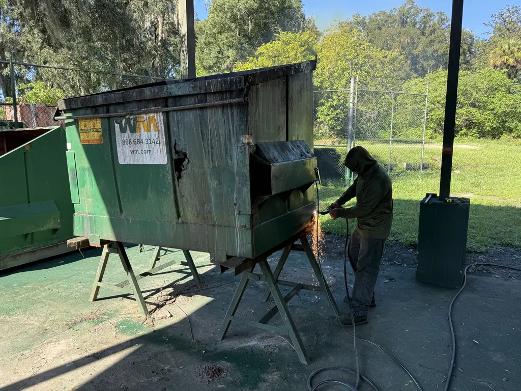 Technician cutting the rusted panel out of a front-load dumpster during welding repair at our Ocala shop