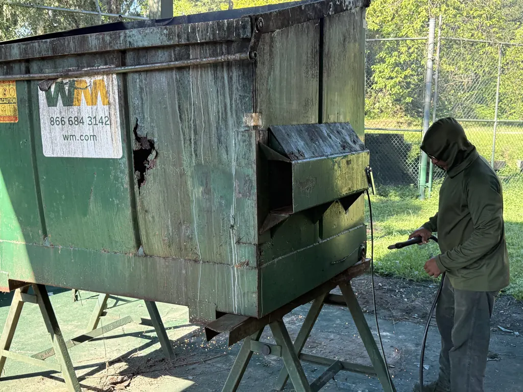 Torch cutting a damaged panel out of a front-load dumpster during welding repair at North Florida Container