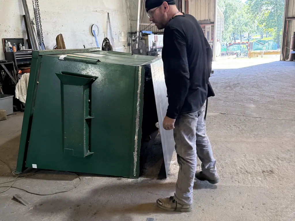 During: technician fitting a new steel floor plate into a front-load dumpster during dumpster floor repair in Ocala FL