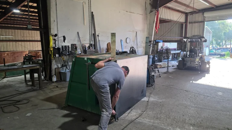 Technician installing new floor panel on front-load dumpster at NFC Ocala shop